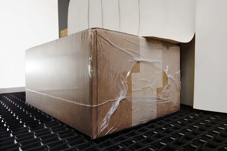 Cardboard box wrapped in plastic on conveyor.
