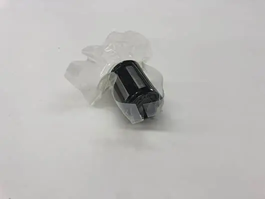 Black cylindrical part in plastic wrap.